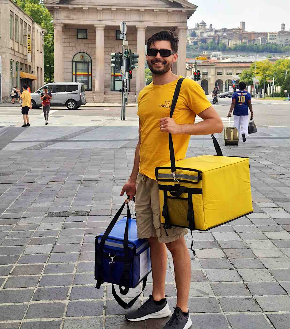 Il ritiro a domicilio LAVACITY in piazza a Bergamo: le due borse gialla e blu del servizio, con Citt&agrave; Alta sullo sfondo